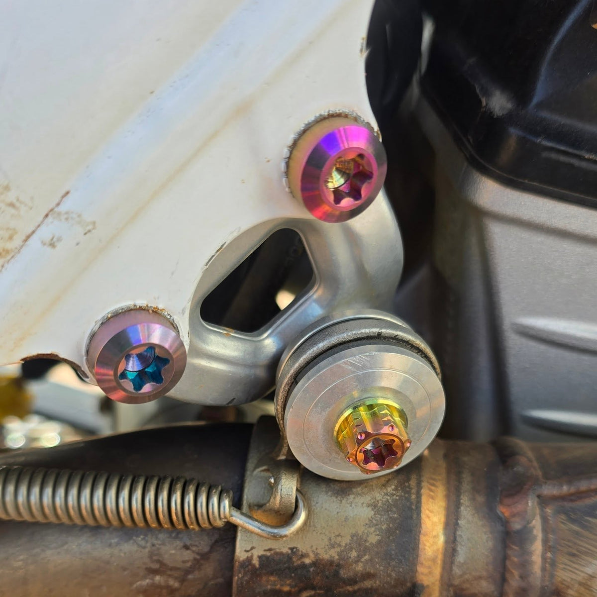 Colored titanium engine mount bracket bolts and an M8x20 exhaust bolt on Isla's white-frame Husqvarna FC 250